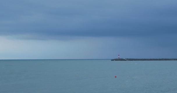 Γλάροι και κορμοράνοι κάθονται σε κυματοθραύστες. Φάρος στο θυελλώδες φόντο του ουρανού. Λιμάνι Σότσι, Ρωσία. — Αρχείο Βίντεο