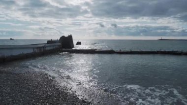 Martılar kayaların ve paslı korkulukların üzerinde otururlar. Gün ışığında sakin deniz sörfü, Sochi, Rusya.