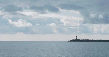 Martılar ve karabataklar dalgakıranların üzerinde otururlar. Bulutlu arka planda deniz feneri. Soçi Limanı, Rusya.