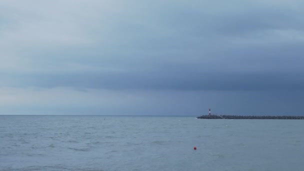 Mewy i kormorany siedzą na falochronie. Latarnia morska na burzliwym tle nieba. Port Soczi, Rosja. — Wideo stockowe