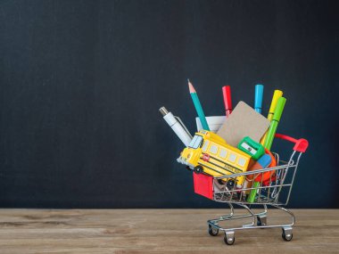 Renkli kırtasiye malzemeleri ve alışveriş arabasında okul otobüsü modeli. Okul konseptine geri dönelim. Fiyat etiketinde kopya alanı olan dikey karatahta arkaplan. Okul alışverişi.