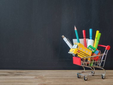 Renkli kırtasiye malzemeleri ve alışveriş arabasında okul otobüsü modeli. Okul konseptine geri dönelim. Kopya alanı olan karatahta arkaplan. Okul alışverişi.