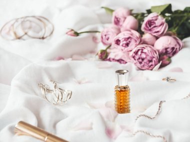 Pembe güller ve buruşuk beyaz kumaş arka planda taç yaprakları. Dekoratif makyaj - parfüm, rimel. Şirin ve şık mücevher aksesuarları..