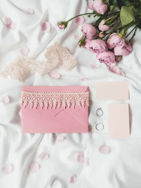 砕いた白い布の上にバラ 自然のエレガントな装飾 結婚指輪とピンクの封筒で招待状と訪問カードとロマンチックな背景 — ストック写真