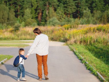 Baba oğlunu okula götürür. Yaz tatilinden sonra okula dönüyorum. Baba ve çocuk el ele yürüyorlar. Aile zamanı, moral desteği.. 