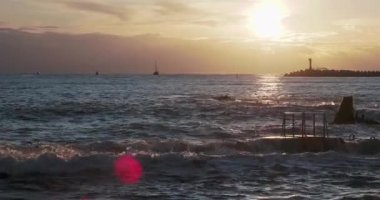 Martılar ve karabataklar dalgakıranların üzerinde otururlar. Muhteşem günbatımı arka planında deniz feneri. Soçi Limanı, Rusya.