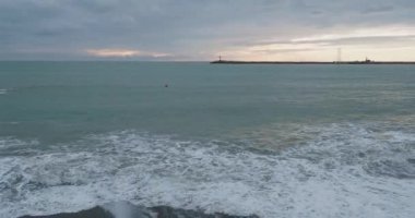 Martılar ve karabataklar dalgakıranların üzerinde otururlar. Günbatımı arka planında deniz feneri. Soçi Limanı, Rusya.