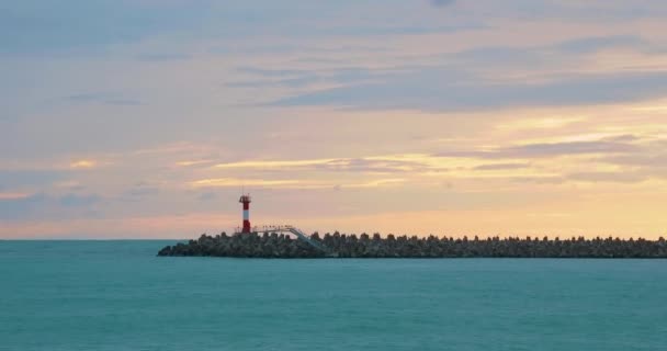 Sirályok és kormoránok ülnek a hullámtörőn. Világítótorony, gyönyörű naplemente háttérrel. Sochi kikötője, Oroszország. — Stock videók