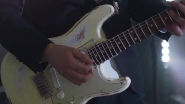 Takım elbiseli bir adam konserde altı telli elektro gitar çalar. Müzisyenlerin ellerindeki flaş disko ışıklarıyla yakın çekim görüntüleri..
