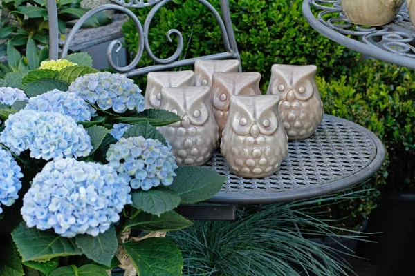 Ceramic owls stand on a chair next to the hydrangea in a flower shop