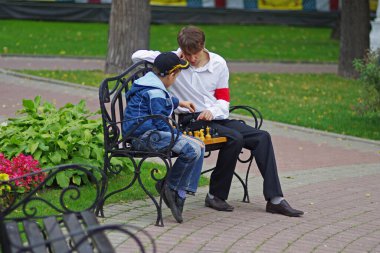Moskova, Rusya - 15 Eylül 2012: Moskova 'daki Hermitage bahçesinde metal bir bankta satranç oynayan genç adam ve çocuk