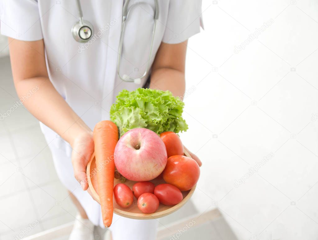 Female doctor nutritionist with fresh apple, tomato, carrot and lettuce in hand Concept of natural food diet nutrition and healthy lifestyle.