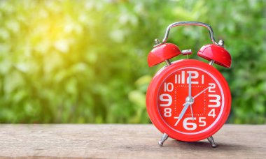 Ahşap masa ve sabah güneşin parlak yeşil arka plan üzerinde kırmızı çalar saat. metin için yer.