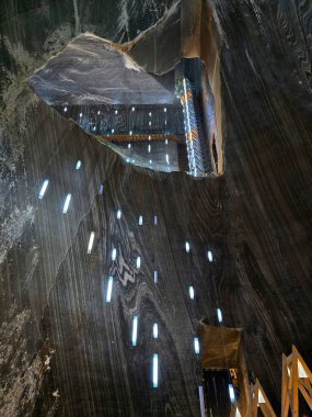 Deep underground Salina Turda salt mine looking up from Mina Terezia trough opening towards Rudolf Gallery with lighted panoramic elevator on the right and wooden high walkway. Salt patterned walls with blue hanging lights. Cluj, Romania