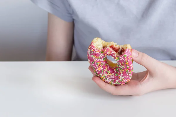 Children\'s hand stretches bitten donut in pink icing and jam filling