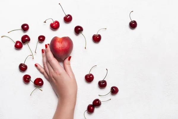 Female hand holds ripe peach on white table. Summer food concept.