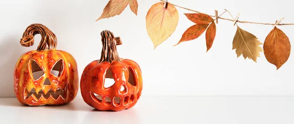 Banner with Ceramic Jack Lanterns and autumn leaves garland on table wall background.