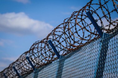 Bulutlu gökyüzüne karşı havalimanını çevreleyen metal ağ çitlerinin tepesindeki dikenli tel.