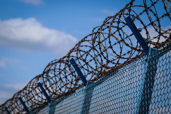 Bulutlu gökyüzüne karşı havalimanını çevreleyen metal ağ çitlerinin tepesindeki dikenli tel.