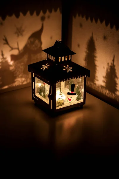 Christmas tea light candle lantern with snowman cast shadows of christmas trees and snow flakes