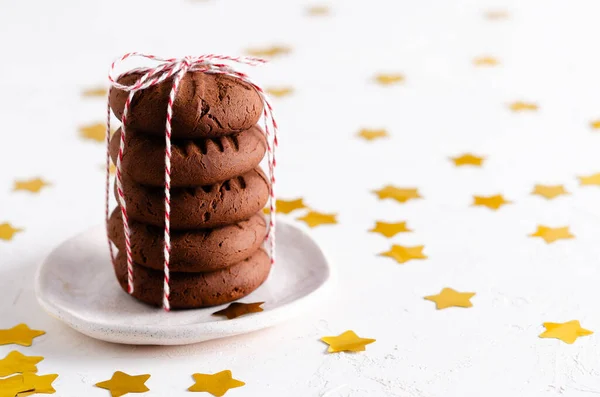 Yığılmış çikolatalı kurabiyeler kırmızı ve beyaz iplikle bağlanmış ve beyaz arka planda altın yıldızlar kopyalanmış..