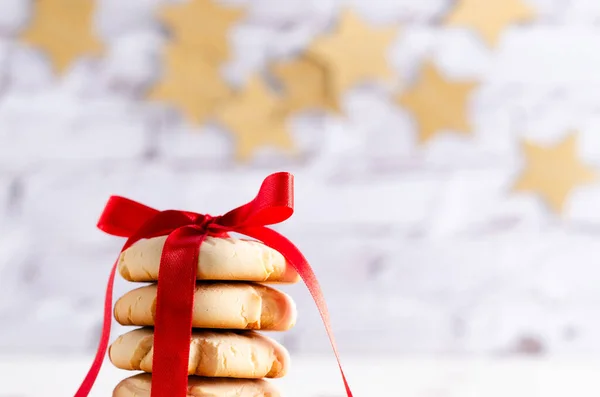 Sırtında kırmızı kurdele ve altın yıldız çelengi olan vanilyalı kurabiyeler yığılmış. Yatay biçim ve kopyalama alanı.
