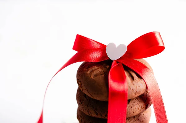 Üstünde kırmızı kurdele ve küçük bir kalp olan çikolatalı kurabiyeler yığılmış. Yatay biçim ve kopyalama alanı.