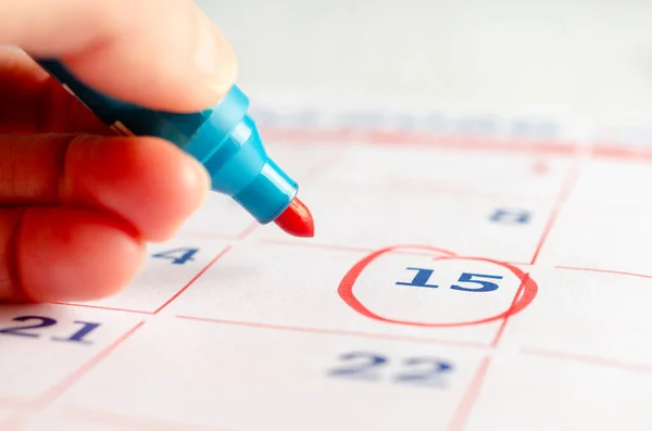 Bir kadın el, takvim sayfasında işaret olan kırmızı bir çember çiziyor. İş konsepti. 