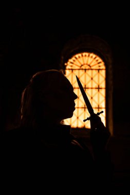 karşı pencere çerçevesinin kale içinde elinde uzun bıçak tutan sarışın kadın silüeti