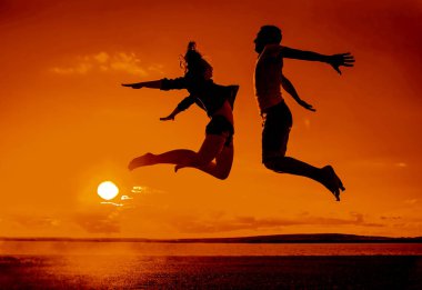 Aile sahilde. Bir çift - erkek ve kadın sahilde günbatımı arka plan atlama silüeti 