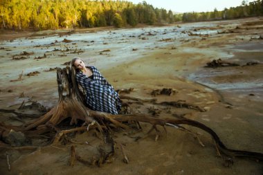 gövde ölü ağaç kökleri üzerinde oturan bir kadın önden görünümü. Derin depresyon kavramı