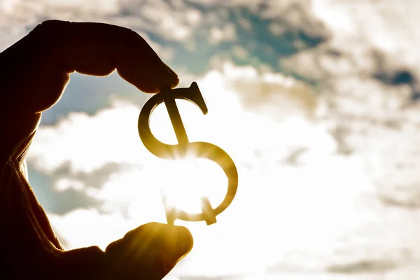 Hand holding  silhouette of dollar sign at sunset background