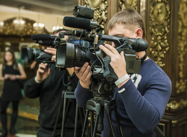 Operator with professional video camcorder on room background.