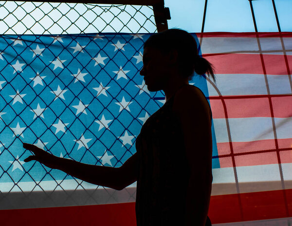 Силуэт африканской американки против американского флага. Большой флаг США, висящий на заборе тюрьмы, силуэт молодой девушки. 4 июля - С Днем памяти
