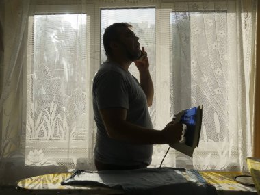 Giyim çamaşır odasında evde Ütü yaparken akıllı telefon kullanan adam