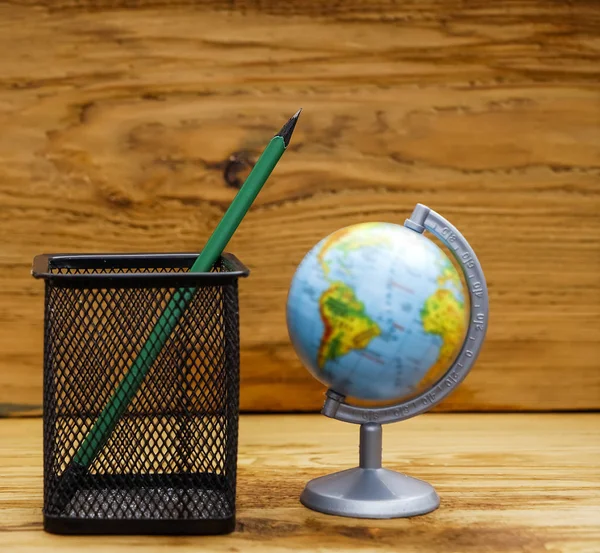 one green pencil in metal net glass and globe against wooden background. back to school