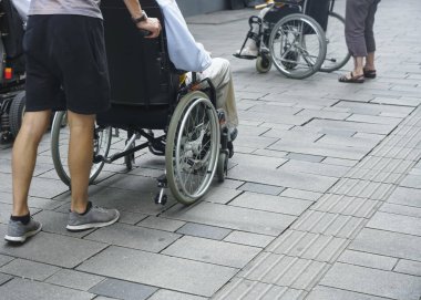 Sokakta tekerlekli sandalyeli engelliler. yüz yok. Tekerlekli sandalyede engelli kadına yardım erkek
