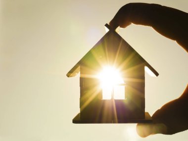 Erkek el tutmak ahşap ev oyuncak güneşli gökyüzü güneş ışınları ile karşı