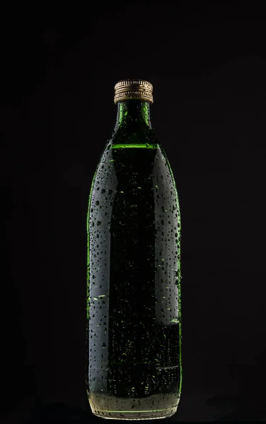 one wet green bottle with mineral pure water isolated on black background. drops on surface.