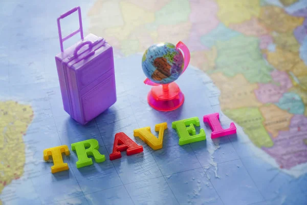 suitcase, globe map and world - travel made from colorful letters lie on world map background.