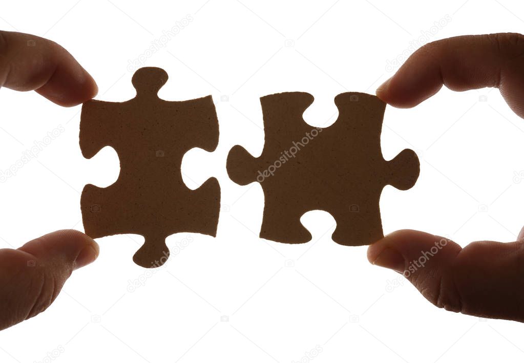 Fingers holding two pieces of brown wooden puzzle. Isolated on white background. 
