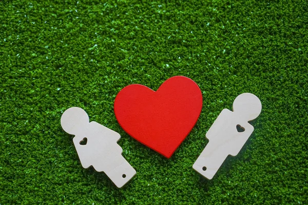 red wooden heart and man, woman concept on green grass background. happy Valentines day idea.