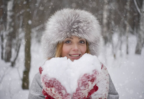 Snow in form of heart. cheerful blond woman in  winter fur hat blowing snow  in winter snowy forest. happy Valentine's Day 