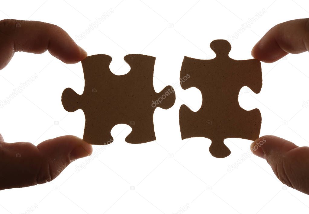 Fingers holding two pieces of brown wooden puzzle. Isolated on white background. 