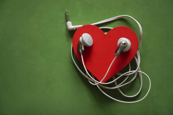 white  earphones on red heart isolated on green  background