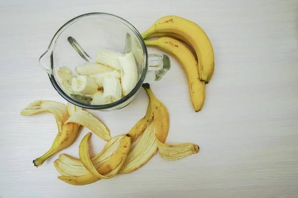Making smoothie, fresh bananas in glass blender jar. top view on wooden table.