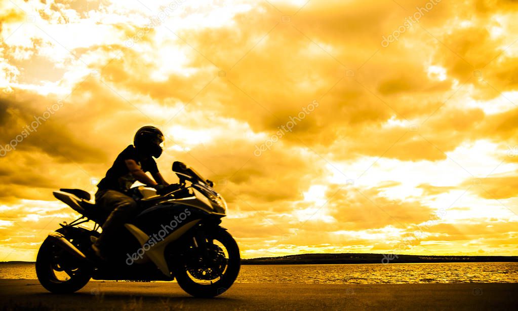 Silhouette of sporty man riding his motorcycle at  sunset. 