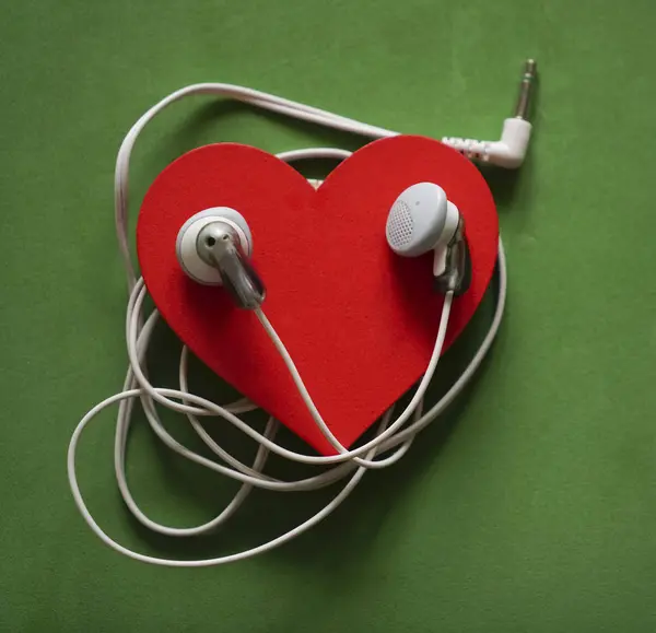 white  earphones on red heart isolated on green  background