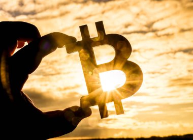günbatımı güneşli gökyüzü bulutlu karşı Bitcoin işaret tutan erkek el. Güneş ışınları.