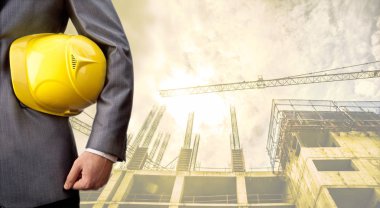 İşçi güvenliği için sarı kask yeni yapı ve inşaat vinçler günbatımı bulutlu gökyüzü akşam arka plan üzerinde arka plan üzerinde tutan mühendisi